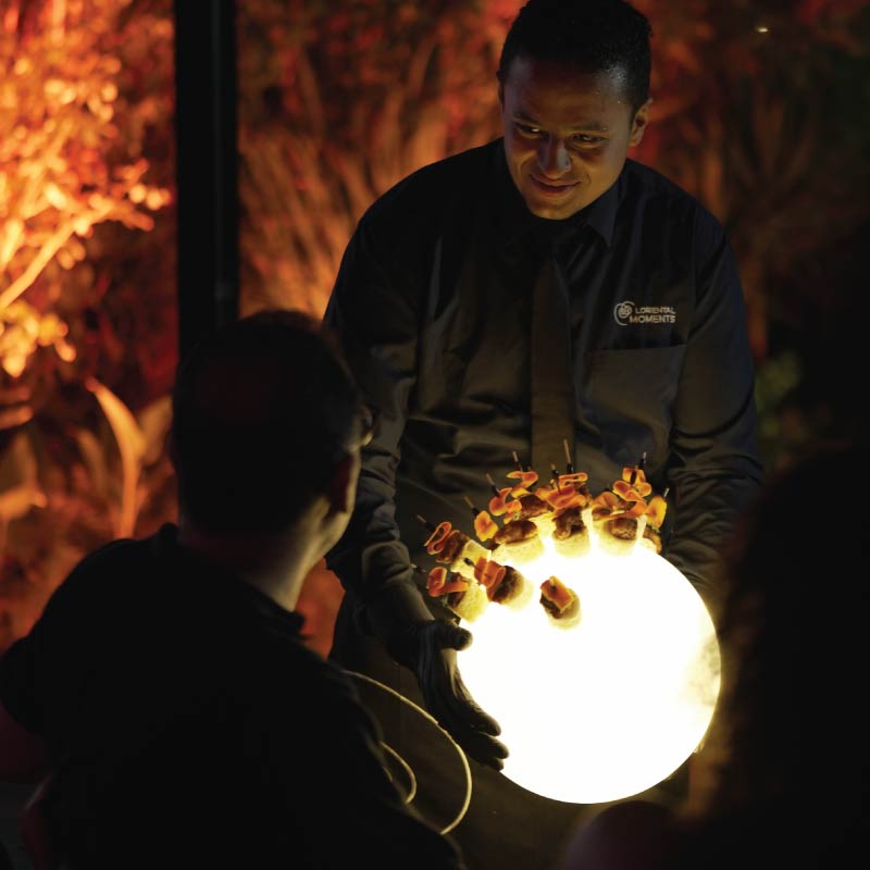 LOriental waiter serving Korean Fried Chicken Bao Bites on theatrical platform Lumisphere