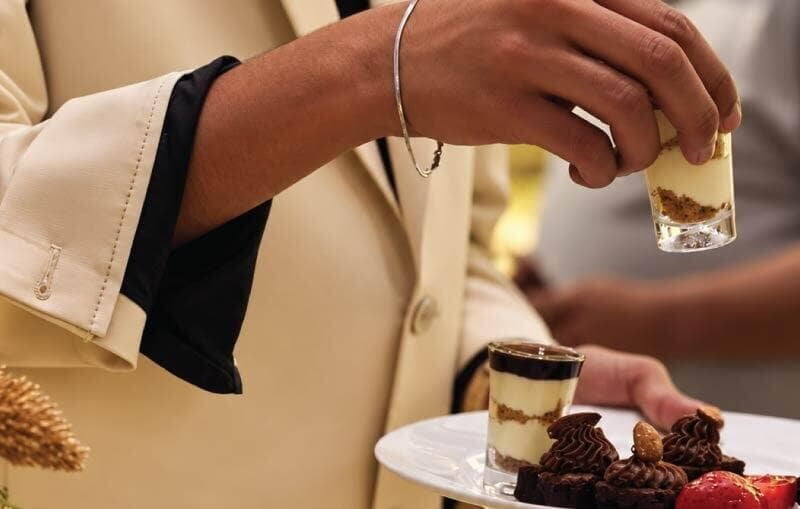 Employee taking tiramisu dirt cups from buffet on plate