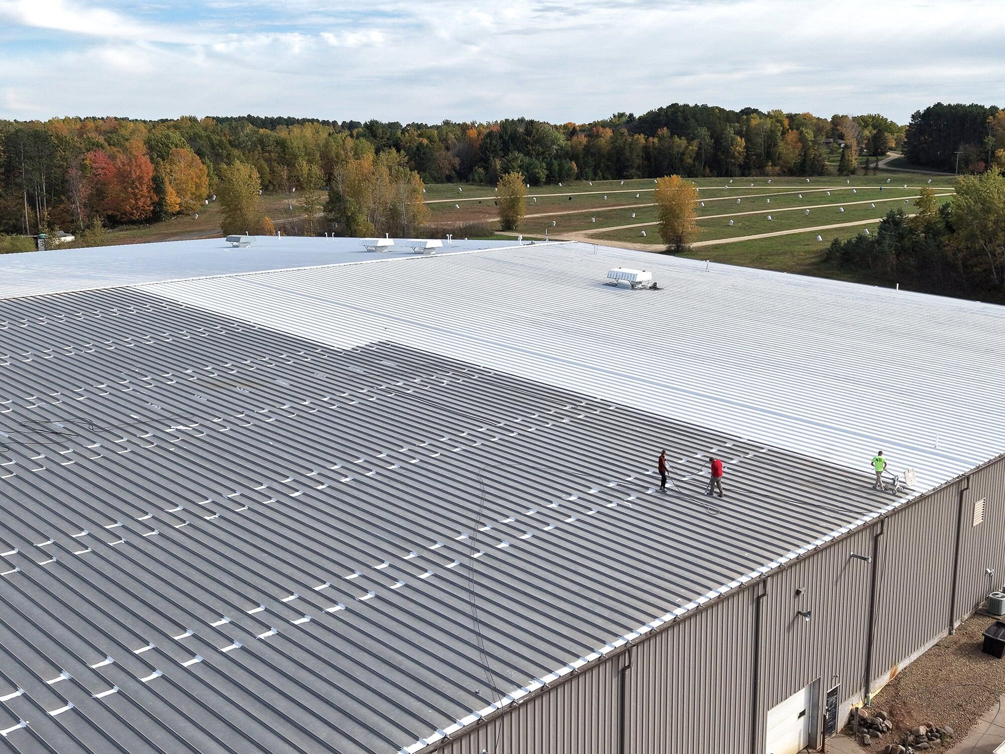 Aerial view of a commercial metal roof with a white coating applied to part of the roof