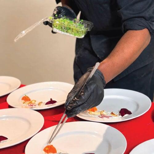LOriental chef adding food garnish to plate