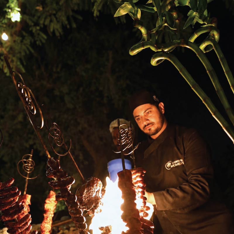 LOriental chef performing live fire cooking with grilled meat at a theatrical culinary station during an event in Egypt LOriental chef performing live fire cooking with grilled meat at a theatrical culinary station during an event in Egypt