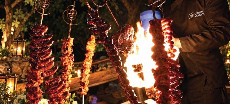 Flaming hanging meat skewers creating a theatrical live cooking experience