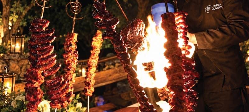 Flame-grilled hanging meat skewers at an interactive live cooking station Flame-grilled hanging meat skewers at an interactive live cooking station