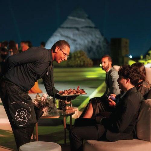 LOriental waiter presenting experiential passaround to Engagement reception guests at Pyramids, photo taken 16 August 2024
