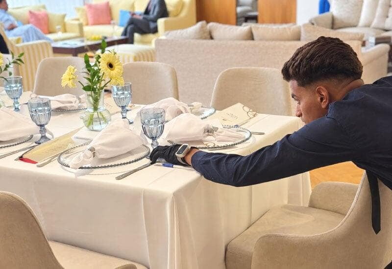 LOriental waiter making final adjustments to table setup at seated event LOriental waiter making final adjustments to table setup at seated event
